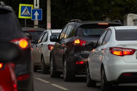 Multiple cars lined up in traffic on a city street with brake lights illuminated and traffic signs visible.