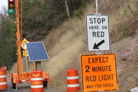 Temporary solar-powered traffic light with signs and orange barrels on a rural roadside during construction.