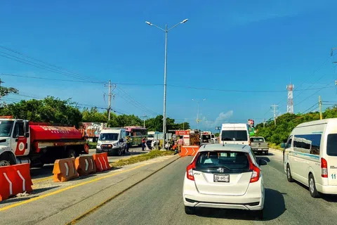 Traffic congestion with multiple vehicles including cars, vans, and a red tanker truck on a sunny day with blue sky.