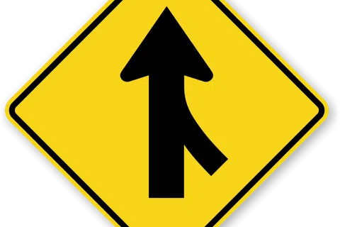 Yellow diamond-shaped traffic sign with black merging lane arrow indicating road merging ahead