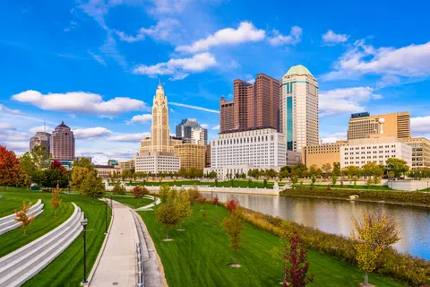 Columbus Ohio skyline with modern buildings, riverfront park, and blue sky on a sunny day.