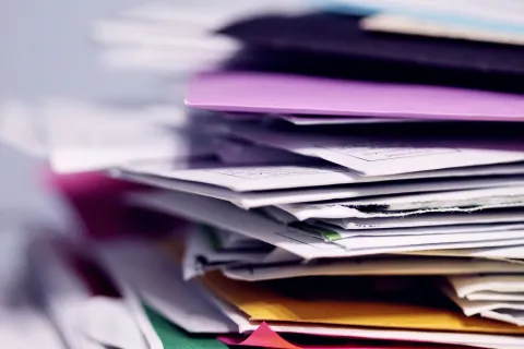 Stack of assorted colorful papers and envelopes piled chaotically on a white surface with a blurred background