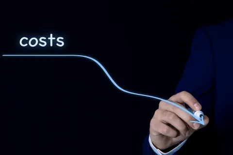 Businessman in suit drawing a glowing blue line pointing downward labeled costs on black background