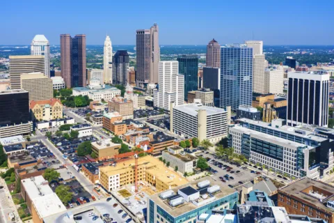 Aerial view of a city skyline with tall buildings under a clear blue sky on a sunny day.