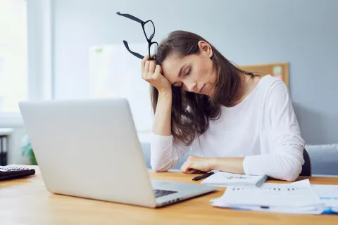 Tired woman sitting at desk showing signs of work-related stress and fatigue in an office setting