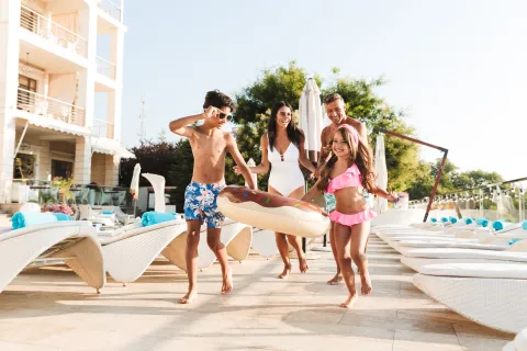 Family enjoying poolside fun with inflatable donut float and sun loungers at resort on a sunny day