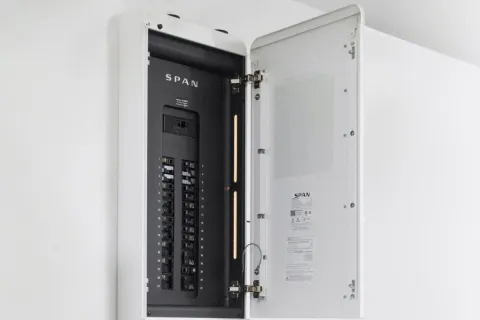 Open SPAN electrical panel with switches and circuit breakers mounted on a white wall