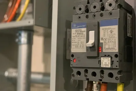 Close-up of an industrial circuit breaker mounted on a wall with connected colored wires.