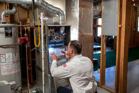 HVAC technician examining a furnace in a residential basement with tools and equipment.