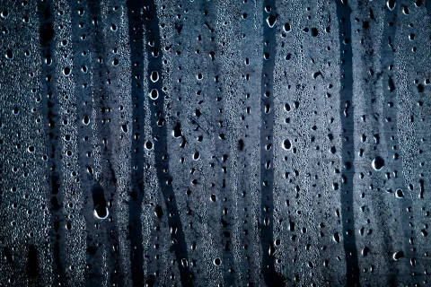 Close-up of water droplets on a glass surface with a dark, textured background.