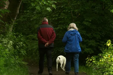 a man and woman walking a dog on a trail in the woods