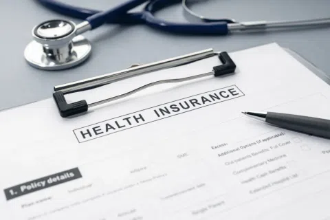 Health insurance form on clipboard with pen and stethoscope on gray surface.