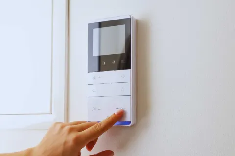 Hand pressing a button on a modern white wall-mounted control panel with a digital screen.