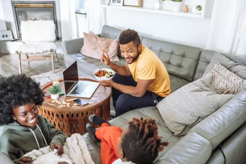 Happy family enjoying time together in cozy living room with laptop and meal on wooden coffee table