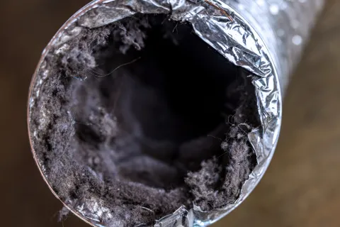 Close-up of a heavily dust-clogged dryer vent duct with visible lint buildup inside.