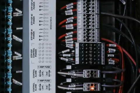 Close-up of an electrical panel with circuit breakers, labeled wires, and indicator lights glowing orange.