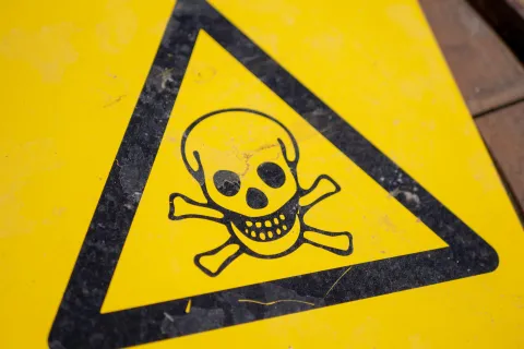 Close-up of a yellow warning sign with a black skull and crossbones indicating toxic or hazardous danger.