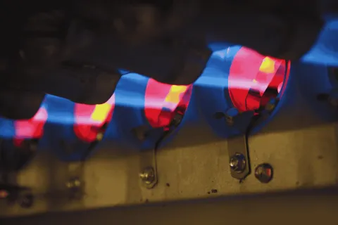 Close-up of multiple blue and red gas flames burning inside a stove burner assembly for cooking.