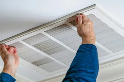 Person removing or installing a white ceiling air vent cover in a home interior.