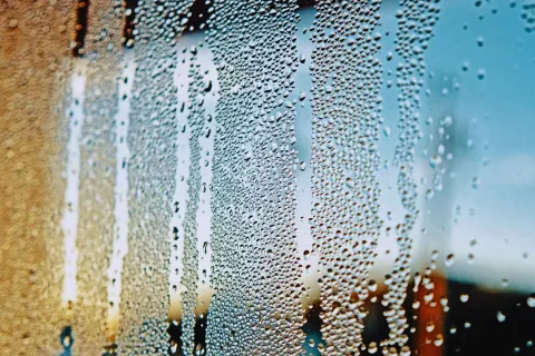 Close-up of water droplets on a window glass with blurred outdoor background in warm and cool tones.