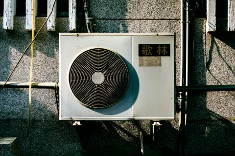 Outdoor air conditioning unit mounted on textured gray wall with shadows and Chinese characters label.