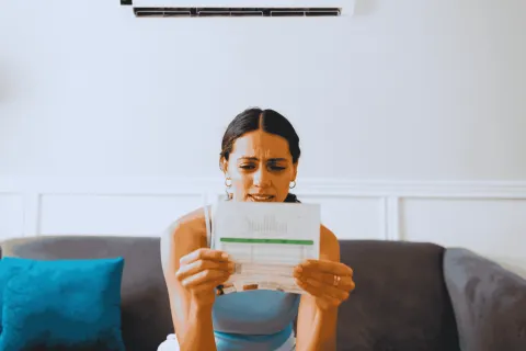 Worried woman sitting on couch reading an unexpected bill or financial statement at home.
