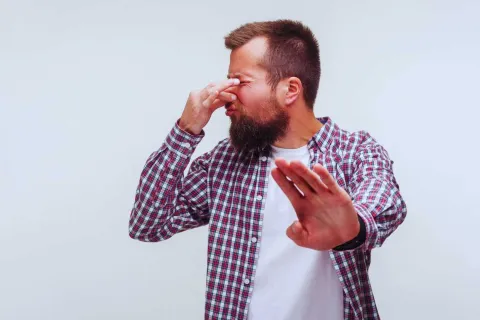 Man in plaid shirt pinching nose and raising hand, reacting to a bad smell or unpleasant odor.