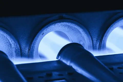 Close-up of blue gas flames burning inside a metal gas burner with pipes and vents glowing under heat.