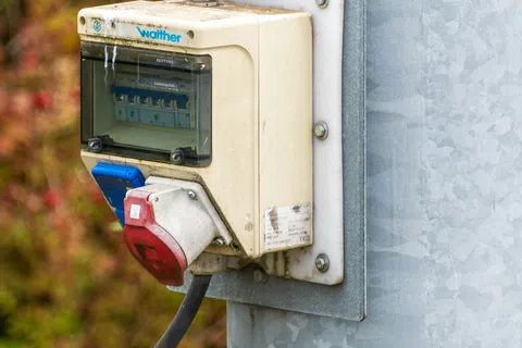 Outdoor electrical junction box with switches and industrial power plugs mounted on a metal pole.
