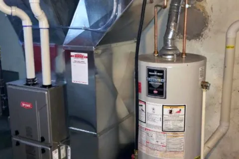A furnace and water heater installed in a basement with visible pipes and ventilation.