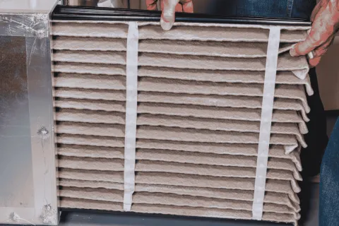 Person replacing or installing a pleated air filter into a HVAC system unit for home air quality.