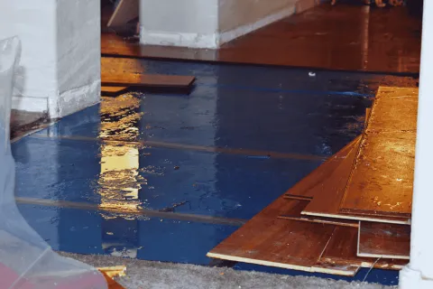 Wet floor with water reflecting light and stacked wooden floor panels ready for installation.
