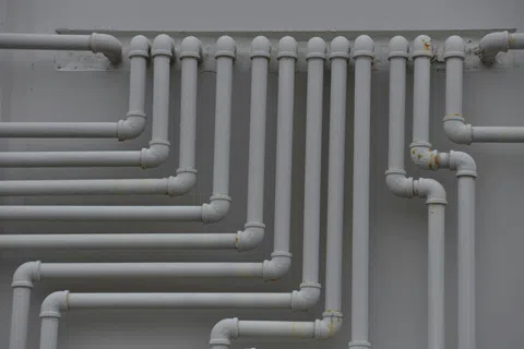 White PVC pipes arranged vertically and horizontally on a gray wall forming a complex plumbing network.