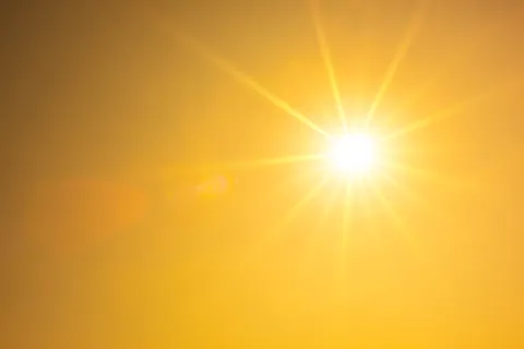 Bright sun with radiant beams shining in a clear yellow-orange sky, evoking warmth and daylight.