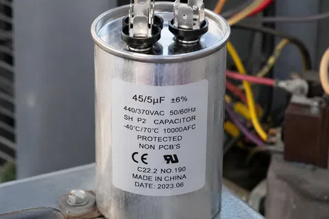 Silver cylindrical capacitor with specifications label and electrical terminals inside an HVAC unit.