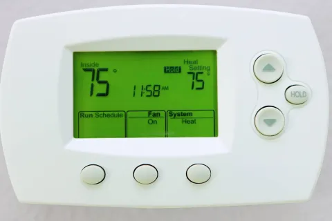 Digital thermostat showing inside temperature 75 degrees, heat setting 75 degrees, fan on, system heat.