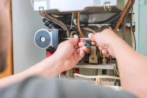 Technician using a wrench to repair or maintain an open boiler or furnace with visible pipes and wiring.