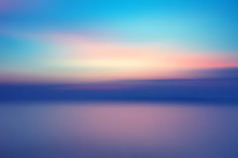 Soft gradient sunrise over calm ocean waters with tranquil blue, pink, and purple hues blending smoothly.