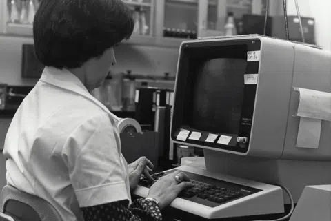 Woman in a lab coat working on a vintage computer showcasing aging IT technology in healthcare.