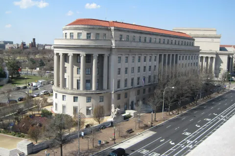 Home of the federal trade commission (FTC), the historic Apex building has columns and red roof beside a wide street.