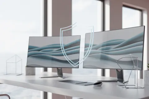 Modern dual monitors on white desk with keyboard, mouse, and digital shield icon representing cybersecurity.