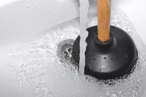 Close-up of a black plunger in a white sink with running water clearing a drain.