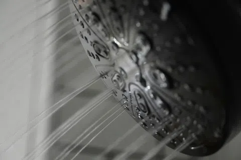 Close-up of a metal showerhead with water streams flowing out against a gray background.