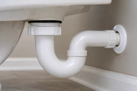 Close-up of a white PVC P-trap drain pipe connected under a bathroom sink against tiled floor