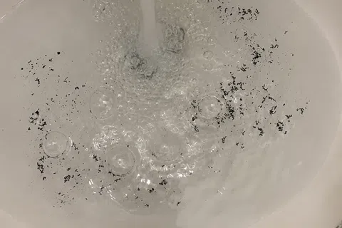 Running water filling a white sink with black debris floating in the water.
