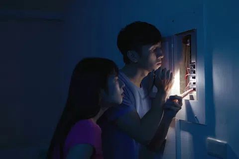 Couple inspecting electrical panel with flashlight in dark room during power outage or repair.
