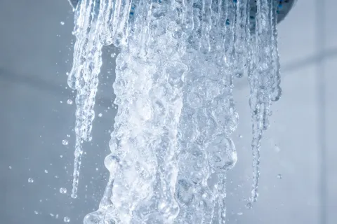 Close-up of water flowing from a silver showerhead against a tiled bathroom wall, creating bubbly streams.