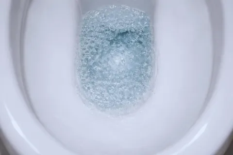Close-up of water swirling and bubbles inside a flushing white ceramic toilet bowl.
