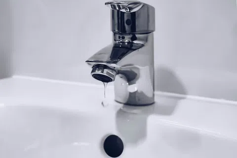 Close-up of a silver faucet dripping water over a white sink with a simple background.