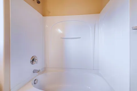 Clean white bathtub with surrounding shower walls and silver faucet and showerhead in beige bathroom.